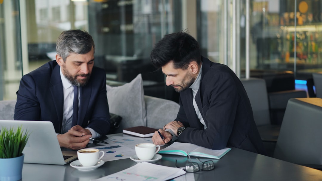 two-men-sitting-at-a-table-working-on-a-laptop-biciz2eskia